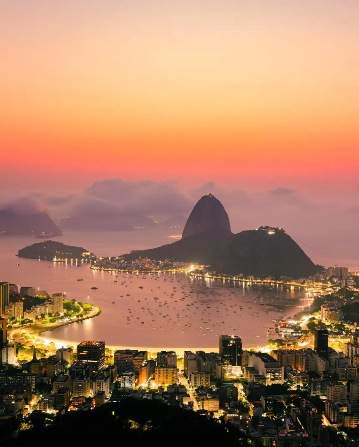 Vista aérea do Pão de Açúcar e da enseada de Botafogo ao entardecer, com barcos na baía